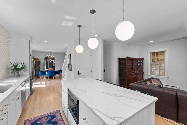 2530 W Morse Ave, Chicago, IL 60645 - kitchen with appliances with stainless steel finishes, a chandelier, a center island, light wood finished floors, and white cabinetry