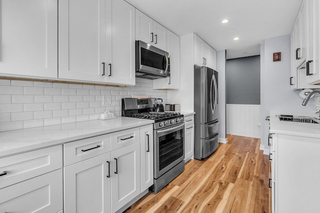 86611/2 W Foster Ave Unit 3A, Chicago, IL 60656 - kitchen featuring stainless steel appliances, a sink, a wainscoted wall, white cabinets, and light wood-style flooring