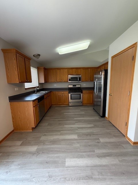 916 Bluegrass Ln, Plano, IL 60545 - kitchen featuring appliances with stainless steel finishes, vaulted ceiling, light wood-style flooring, brown cabinetry, and dark countertops