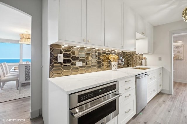 1440 N Lake Shore Dr Unit 34Ac, Chicago, IL 60610 - kitchen featuring a sink, appliances with stainless steel finishes, decorative backsplash, light wood-style flooring, and light stone countertops