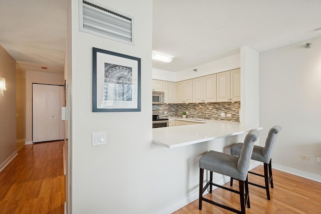 512 N Mcclurg Ct Unit 1009, Chicago, IL 60611 - kitchen featuring appliances with stainless steel finishes, cream cabinetry, a kitchen breakfast bar, tasteful backsplash, and light wood finished floors