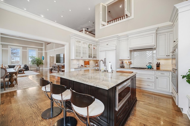 201 Reber St Unit 6, Wheaton, IL 60187 - kitchen with built in appliances, a breakfast bar, glass insert cabinets, decorative backsplash, and light wood-style flooring