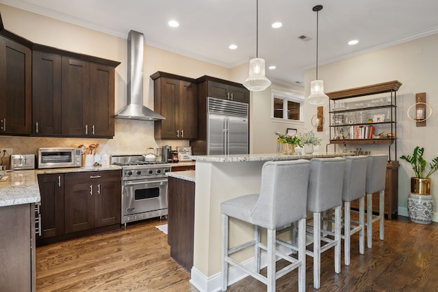 663 W Wellington Ave Unit 1, Chicago, IL 60657 - kitchen featuring high quality appliances, wall chimney range hood, dark brown cabinets, a breakfast bar area, and ornamental molding