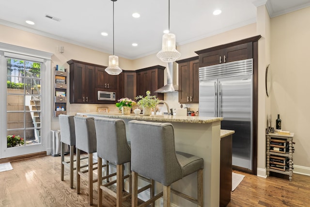 663 W Wellington Ave Unit 1, Chicago, IL 60657 - kitchen featuring appliances with stainless steel finishes, wall chimney range hood, dark brown cabinetry, backsplash, and ornamental molding