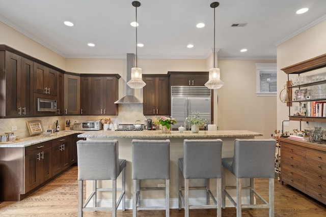 663 W Wellington Ave Unit 1, Chicago, IL 60657 - kitchen featuring appliances with stainless steel finishes, wall chimney range hood, dark brown cabinetry, a breakfast bar, and backsplash