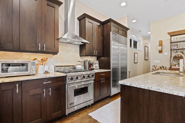 663 W Wellington Ave Unit 1, Chicago, IL 60657 - kitchen featuring wall chimney range hood, premium appliances, a sink, dark brown cabinetry, and tasteful backsplash