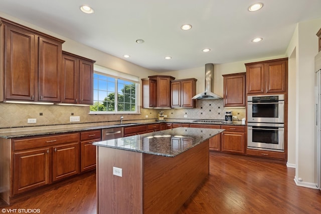 2621 Hastings Ct, Gurnee, IL 60031 - kitchen with wall chimney range hood, appliances with stainless steel finishes, dark wood-style floors, a kitchen island, and dark stone countertops