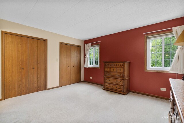 bedroom with two closets, light carpet, and baseboards