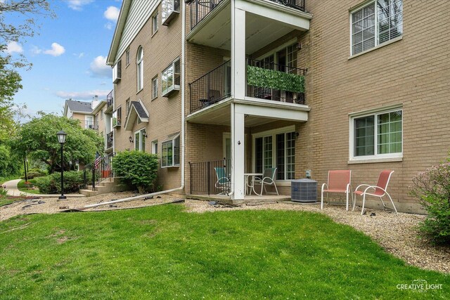 back of house with brick siding, a balcony, and a lawn
