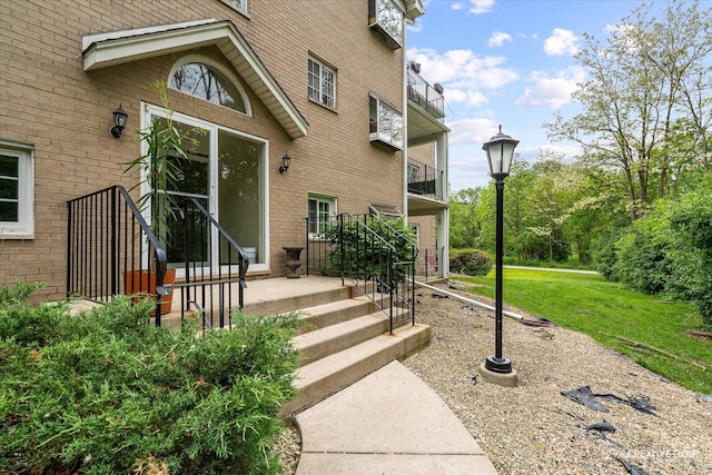 entrance to property featuring brick siding, a yard, and a balcony