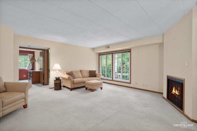 carpeted living room featuring a textured ceiling and a warm lit fireplace