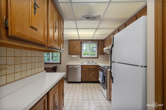 kitchen with white appliances, brown cabinets, a sink, a drop ceiling, and light flooring