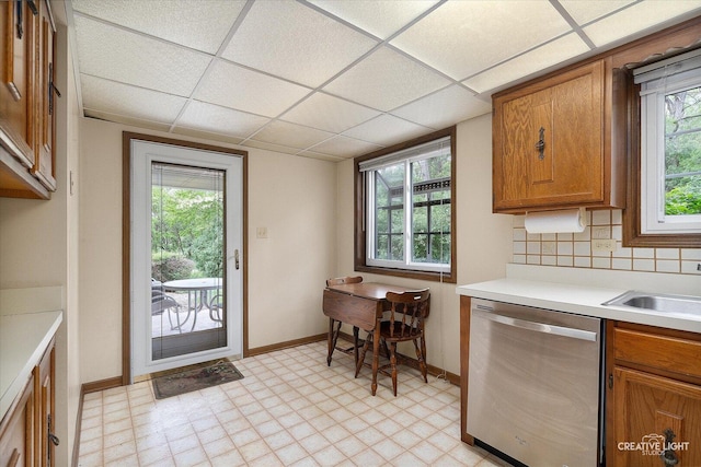 kitchen featuring stainless steel dishwasher, brown cabinetry, light flooring, light countertops, and baseboards