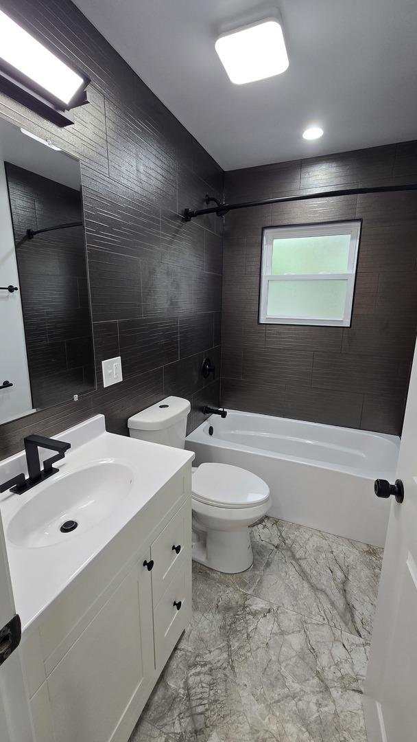 full bath with vanity,  shower combination, toilet, and marble finish flooring
