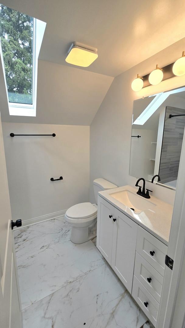 bathroom with a skylight, marble look tile flooring, vanity, toilet, and lofted ceiling