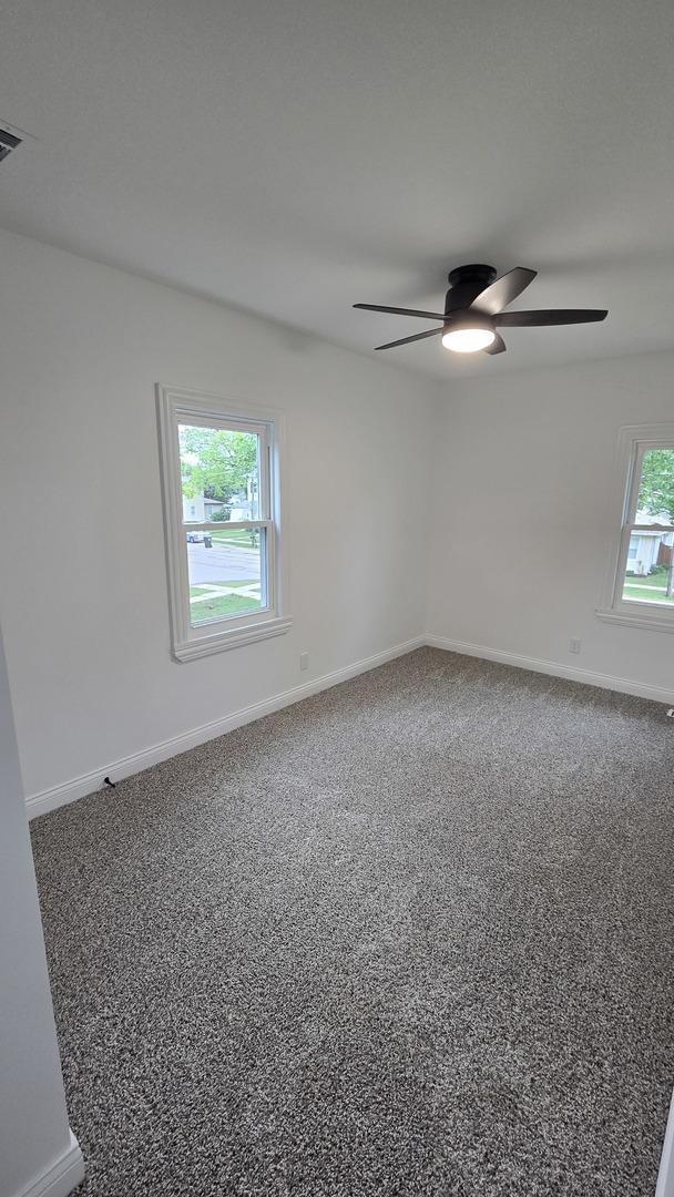 carpeted empty room with a ceiling fan and baseboards