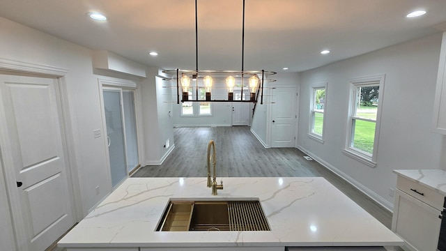unfurnished dining area with dark wood-type flooring, a sink, baseboards, recessed lighting, and a chandelier
