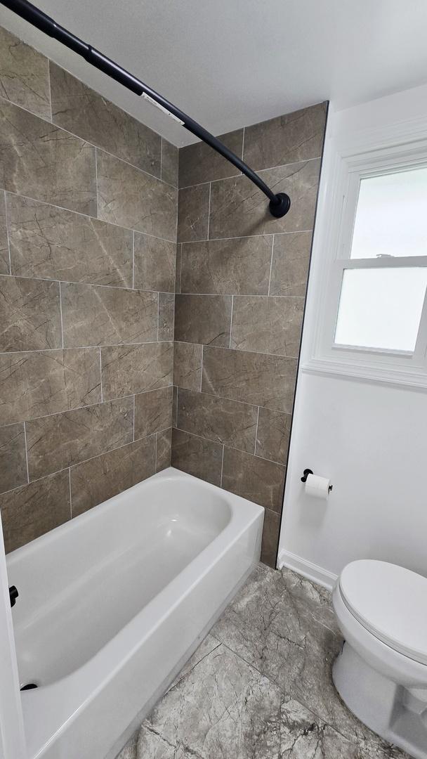 full bath featuring toilet, marble finish floors, baseboards, and shower / washtub combination