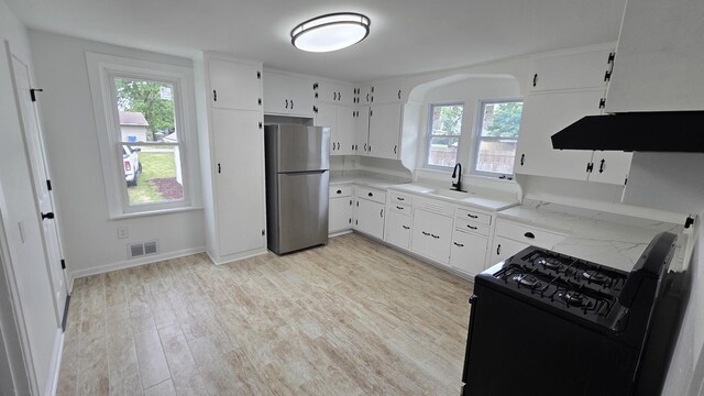kitchen featuring freestanding refrigerator, black gas range oven, a sink, and plenty of natural light