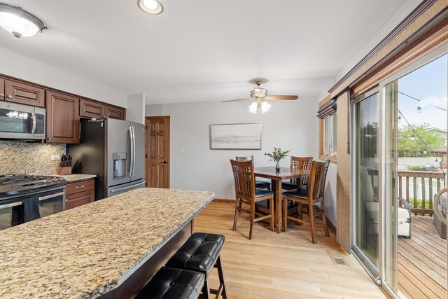 13641 W Ironwood Cir, Homer Glen, IL 60491 - kitchen featuring appliances with stainless steel finishes, a breakfast bar area, backsplash, light wood-style floors, and a ceiling fan