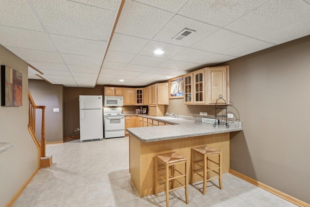 11624 Kluth Ct, Mokena, IL 60448 - kitchen with white appliances, light brown cabinetry, a drop ceiling, glass insert cabinets, and a peninsula