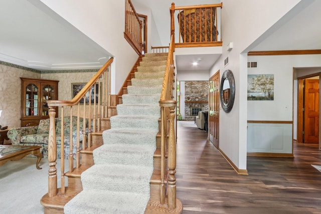 11624 Kluth Ct, Mokena, IL 60448 - stairway featuring wood finished floors, wallpapered walls, ornamental molding, a towering ceiling, and a brick fireplace