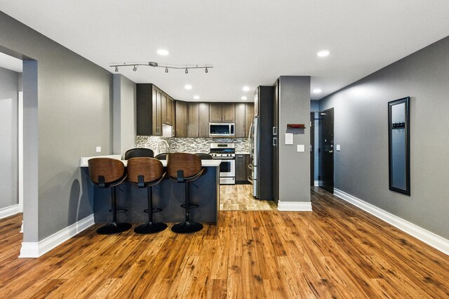1258 Brown St Unit 204, Des Plaines, IL 60016 - kitchen featuring appliances with stainless steel finishes, wood finished floors, a peninsula, decorative backsplash, and rail lighting