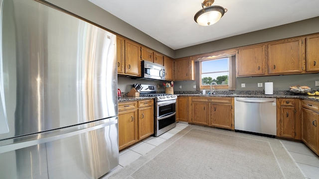 3894 E Whippoorwill Ln, Byron, IL 61010 - kitchen with appliances with stainless steel finishes, a sink, brown cabinetry, dark stone counters, and light tile patterned flooring