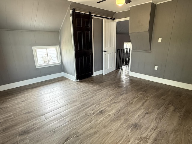 302 E Carroll St, Lanark, IL 61046 - spare room featuring a barn door, a ceiling fan, dark wood-style flooring, baseboards, and wood walls