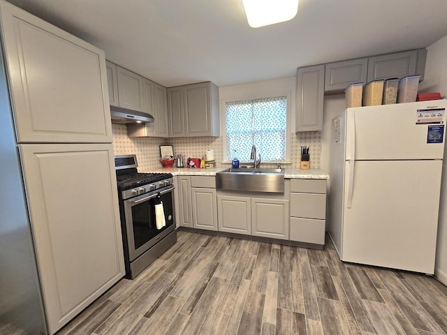 108 E Washington St, Ashkum, IL 60911 - kitchen with freestanding refrigerator, stainless steel gas stove, a sink, under cabinet range hood, and light wood finished floors