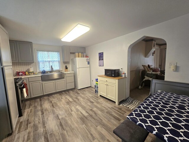 108 E Washington St, Ashkum, IL 60911 - kitchen featuring freestanding refrigerator, a sink, black microwave, arched walkways, and light wood-style flooring
