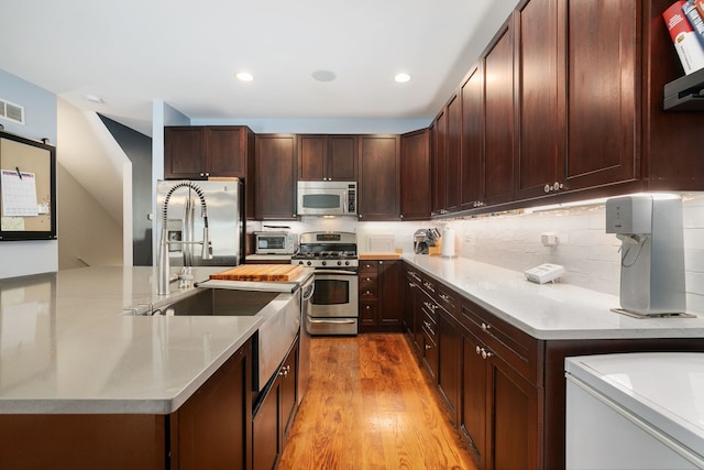 1828 N California Ave, Chicago, IL 60647 - kitchen featuring stainless steel appliances, light countertops, wood finished floors, a center island with sink, and decorative backsplash