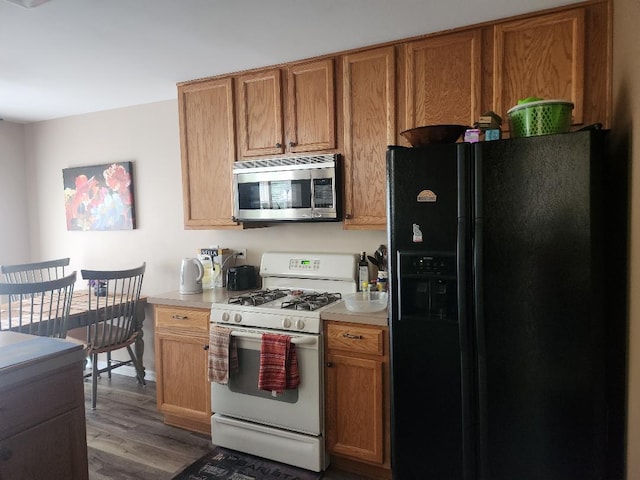 152 W Chatham Ln, Round Lake, IL 60073 - kitchen featuring stainless steel microwave, black fridge with ice dispenser, gas range gas stove, light countertops, and wood finished floors