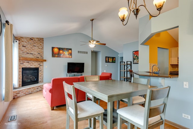 3018 Coastal Dr, Aurora, IL 60503 - dining space with light wood-style flooring, lofted ceiling, a brick fireplace, ceiling fan, and a chandelier