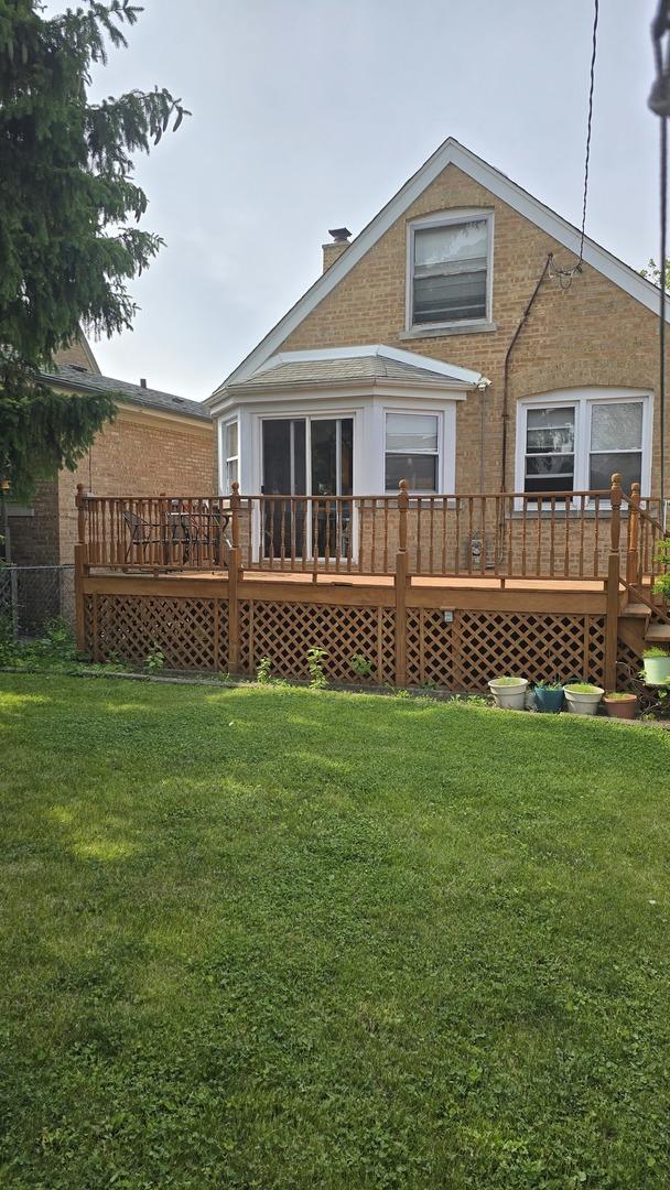 back of property with a wooden deck, a yard, and brick siding