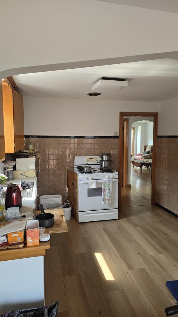 kitchen with white range with gas stovetop, wood finished floors, arched walkways, wainscoting, and tile walls