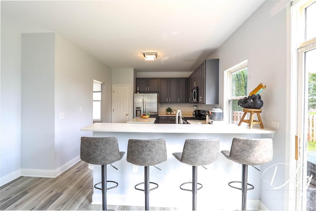 1943 Lily Ln, Round Lake, IL 60073 - kitchen featuring appliances with stainless steel finishes, light wood-style flooring, dark brown cabinets, light countertops, and a breakfast bar