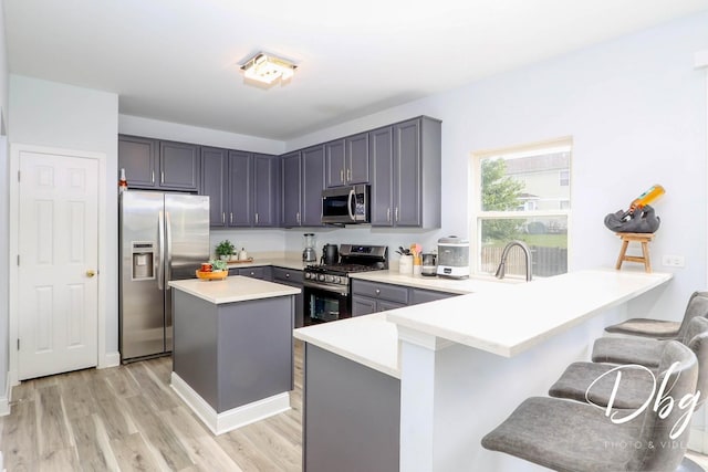 1943 Lily Ln, Round Lake, IL 60073 - kitchen featuring appliances with stainless steel finishes, a peninsula, a kitchen breakfast bar, light wood finished floors, and a center island