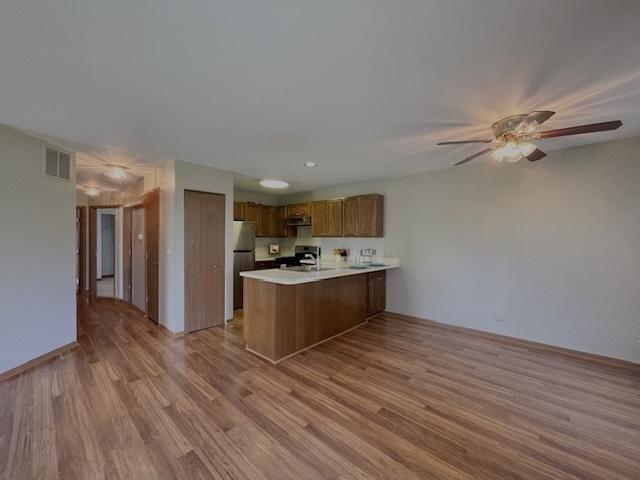 304 University Ln Unit 5, Elk Grove Village, IL 60007 - kitchen featuring freestanding refrigerator, gas range, a peninsula, brown cabinets, and light wood-style floors
