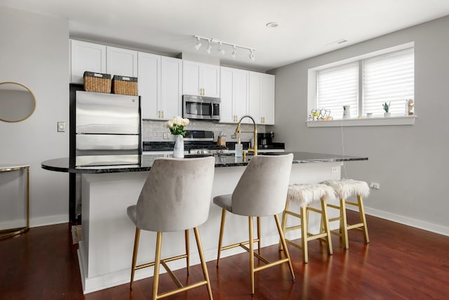 2257 W Lake St Unit 101, Chicago, IL 60612 - kitchen with appliances with stainless steel finishes, an island with sink, decorative backsplash, white cabinets, and baseboards