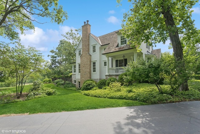 view of front of property featuring a chimney, a front lawn, and covered porch
