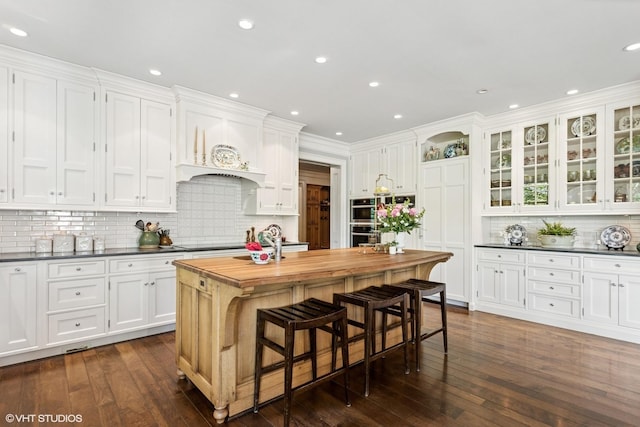 kitchen featuring white cabinets, wooden counters, tasteful backsplash, dark wood-style flooring, and a center island