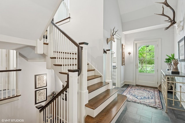 foyer entrance with stairway, stone finish flooring, and vaulted ceiling