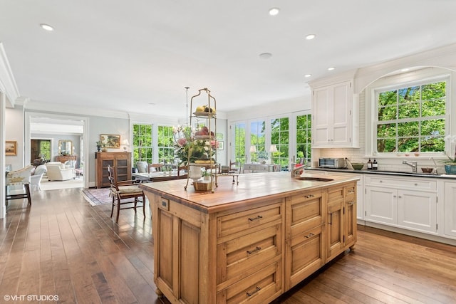 kitchen with a sink, wood-type flooring, crown molding, a center island, and white cabinets