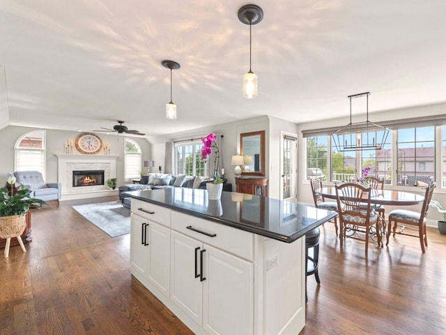 18210 W Winds Ln, Orland Park, IL 60467 - kitchen featuring dark countertops, ceiling fan, a kitchen island, dark wood-style flooring, and a warm lit fireplace