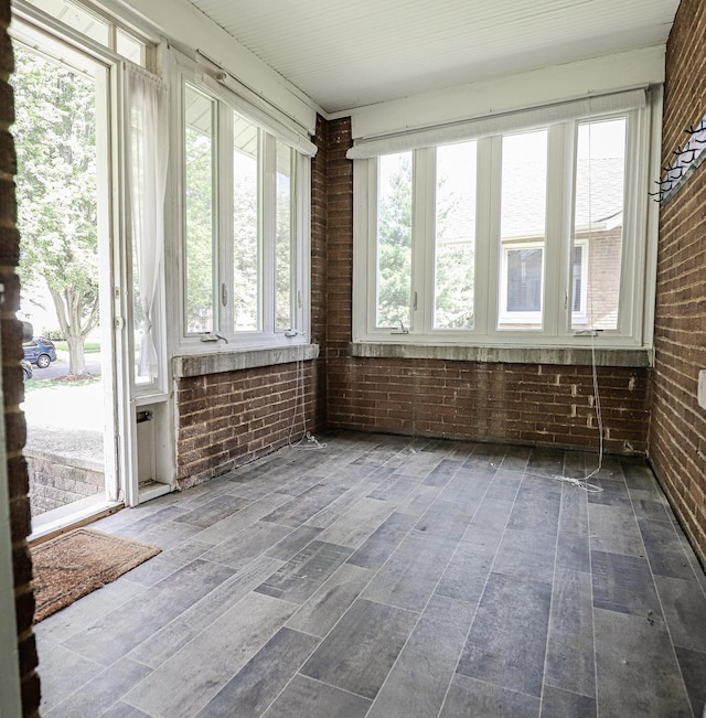 unfurnished sunroom with brick wall, plenty of natural light, and wood finished floors