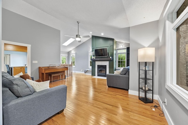 7308 W Lancaster Rd, Peoria, IL 61607 - living area with ceiling fan, a tiled fireplace, light wood-style flooring, vaulted ceiling, and baseboards