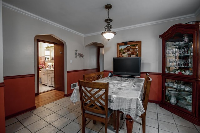 5936 S Keeler Ave, Chicago, IL 60629 - dining area featuring light tile patterned floors, arched walkways, a wainscoted wall, and crown molding