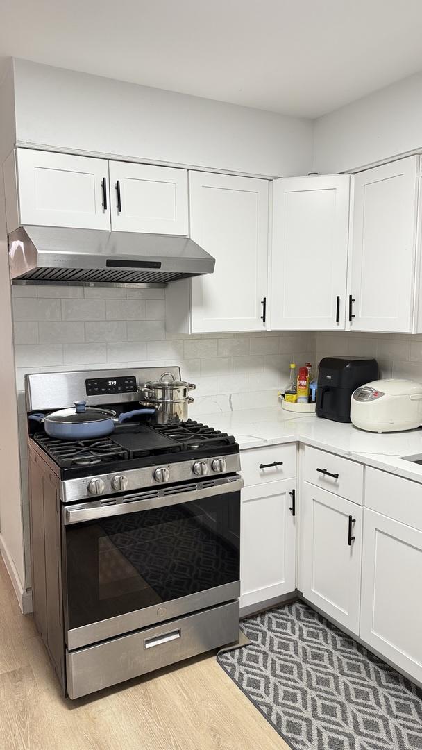 532 W 27th St, Chicago, IL 60616 - kitchen with gas range, wall chimney exhaust hood, light wood finished floors, white cabinets, and light countertops