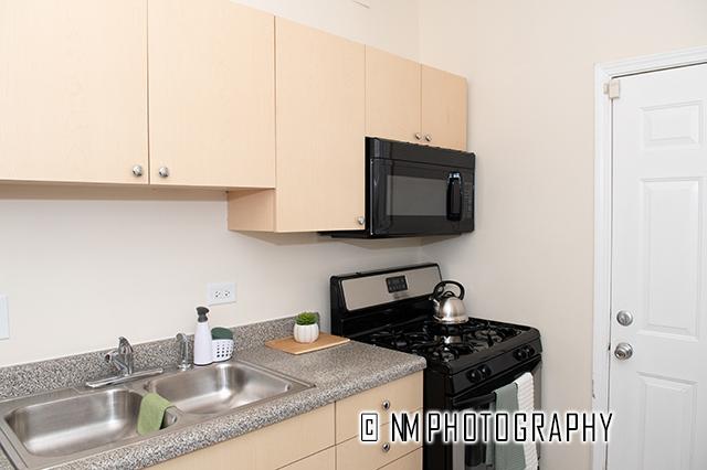 1942 E 74th St Unit 3B, Chicago, IL 60649 - kitchen featuring black microwave, gas range, a sink, cream cabinetry, and light countertops